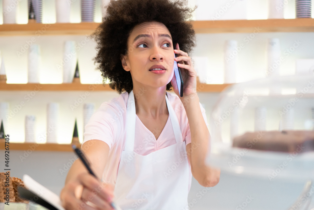 A beautiful mixed-race female worker in a pastry-gelato shop takes an order over the phone and writes it down. A beautiful mixed-race female worker in a pastry-gelato shop takes an order over the phone and writes it down.