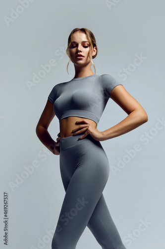 Beautiful young woman with natural make-up and gathered hair, dressed in a gray sports uniform, posing in the studio on a gray background.Advertising sportswear and yoga wear. Healthy lifestyle, sport
