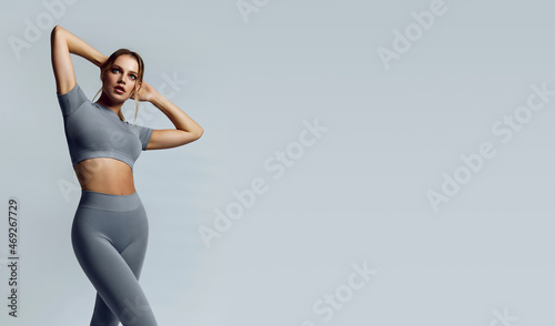 Beautiful young woman with natural make-up and gathered hair, dressed in a gray sports uniform, posing in the studio on a gray background.Advertising sportswear and yoga wear. Healthy lifestyle, sport