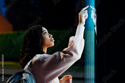 Young woman touching kiosk screen at night photo