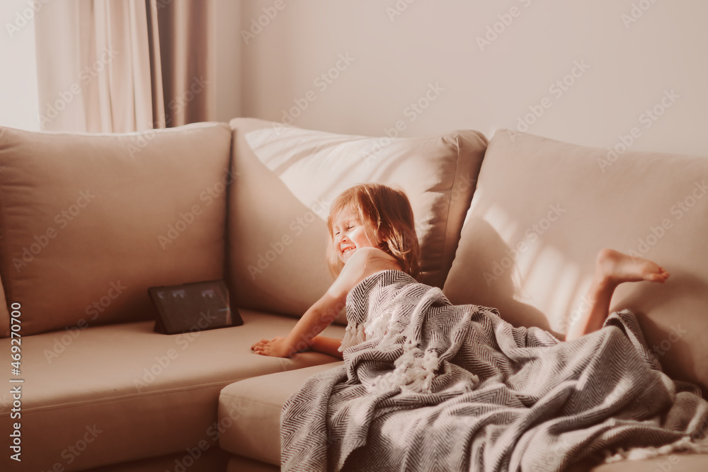 Cute toddler girl lies on beige couch and using laptop tablet pad. Cute toddler girl lies on beige couch and using laptop tablet pad.