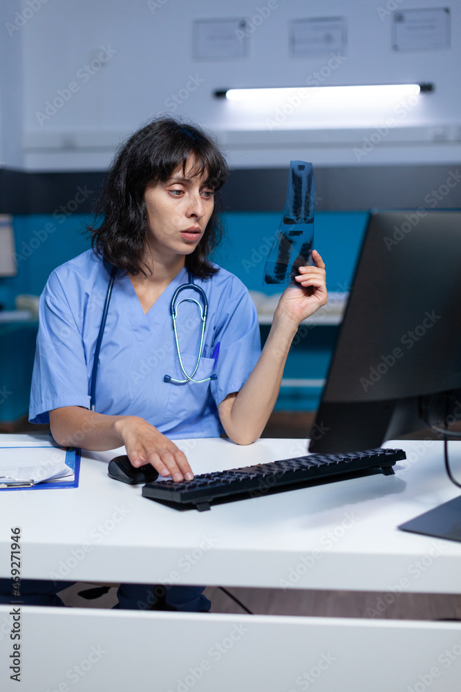 Medical assistant holding x ray scan for examination and diagnosis overtime. Woman nurse analyzing radiography results for healthcare and medical advice, working late at night in cabinet. Medical assistant holding x ray scan for examination and diagnosis overtime. Woman nurse analyzing radiography results for healthcare and medical advice, working late at night in cabinet.