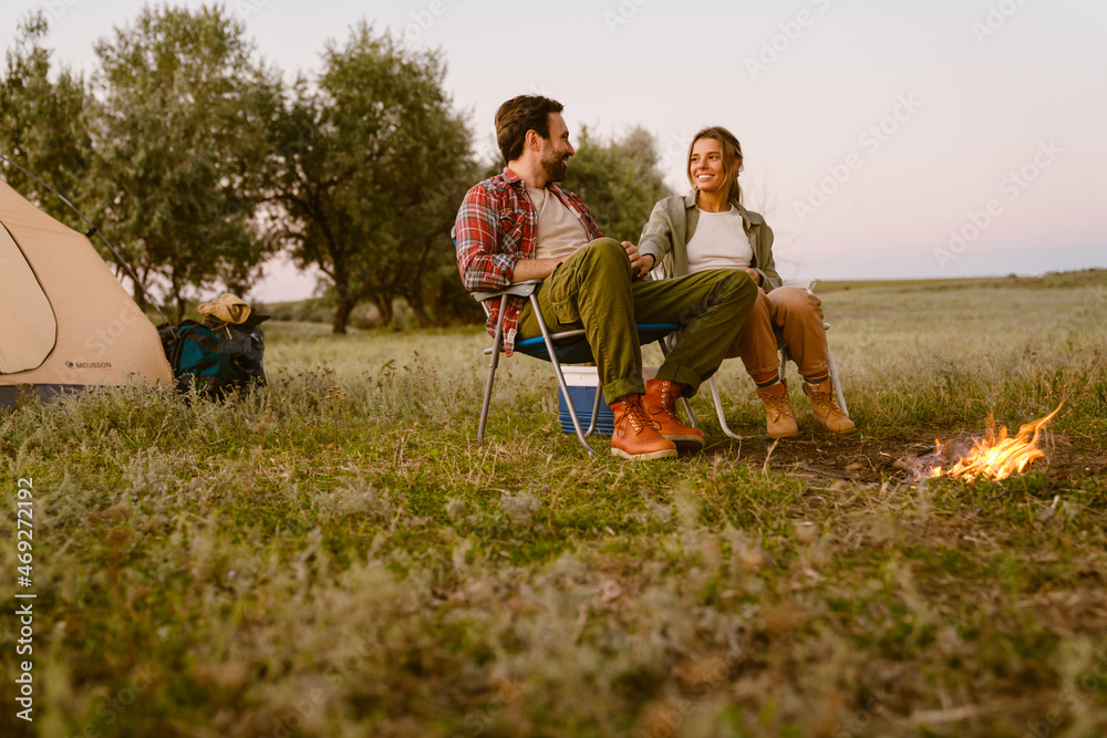 White couple smiling and sitting on chair during camping together White couple smiling and sitting on chair during camping together