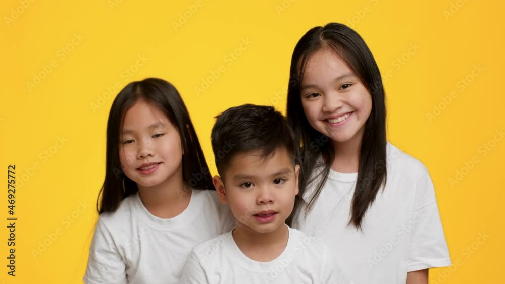 Two Happy Japanese Sisters And Little Brother Posing, Yellow Background Two Happy Japanese Sisters And Little Brother Posing, Yellow Background