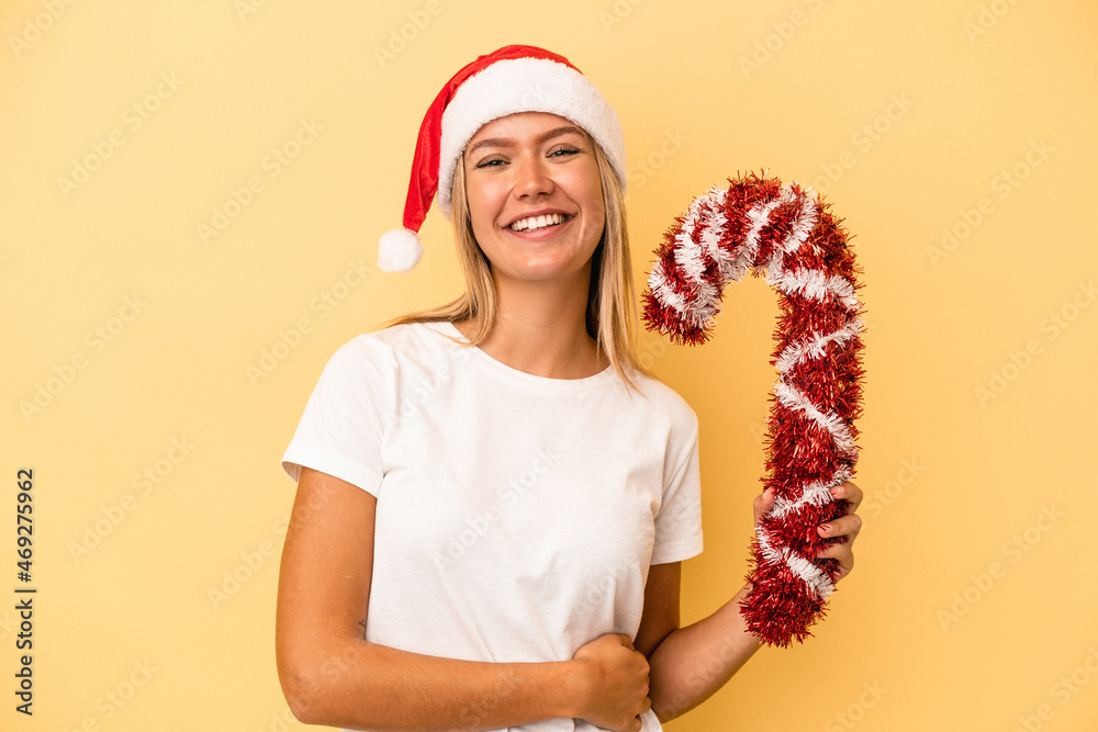 Young caucasian woman holding big christmas stick isolated on yellow background laughing and having fun. Young caucasian woman holding big christmas stick isolated on yellow background laughing and having fun.