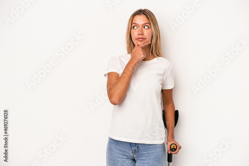 Young caucasian woman holding crutch isolated on white background looking sideways with doubtful and skeptical expression. photo