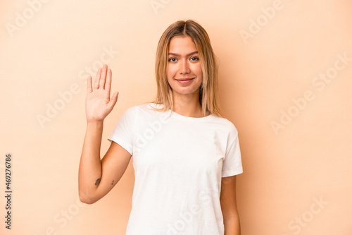 Young caucasian woman isolated on beige background smiling cheerful showing number five with fingers.