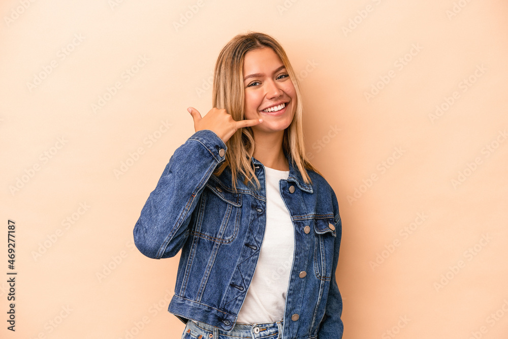 Young caucasian woman isolated on beige background showing a mobile phone call gesture with fingers. Young caucasian woman isolated on beige background showing a mobile phone call gesture with fingers.