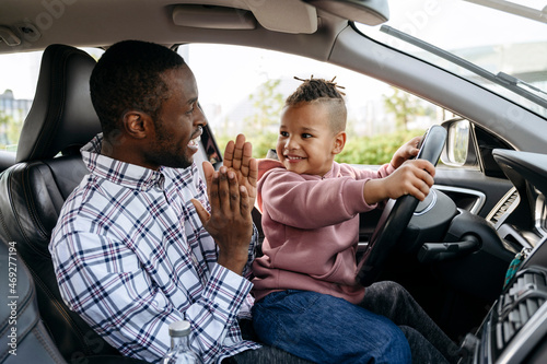 Man clapping hands for son playing with steering wheel in car photo