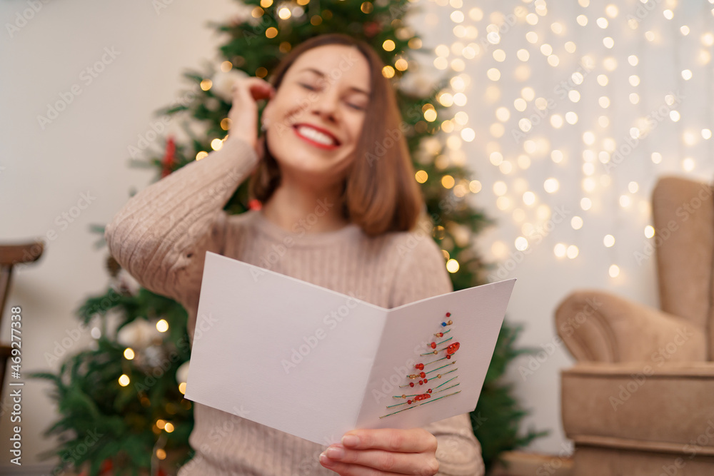 Beautiful woman laughing while reading a Christmas greeting card with light in background. Copy space for text. Beautiful woman laughing while reading a Christmas greeting card with light in background. Copy space for text.