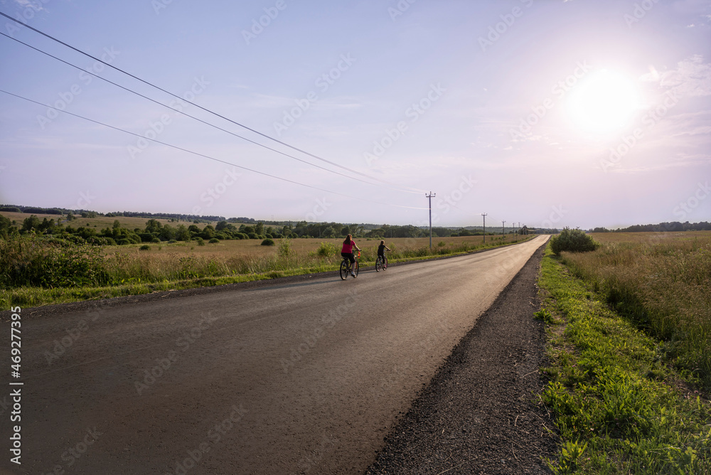 Two cyclists are riding on a rural road