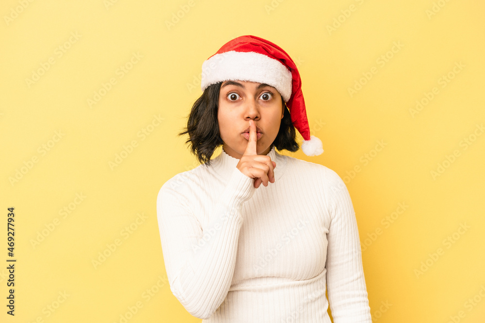 Young latin woman celebrating christmas isolated on yellow background keeping a secret or asking for silence.