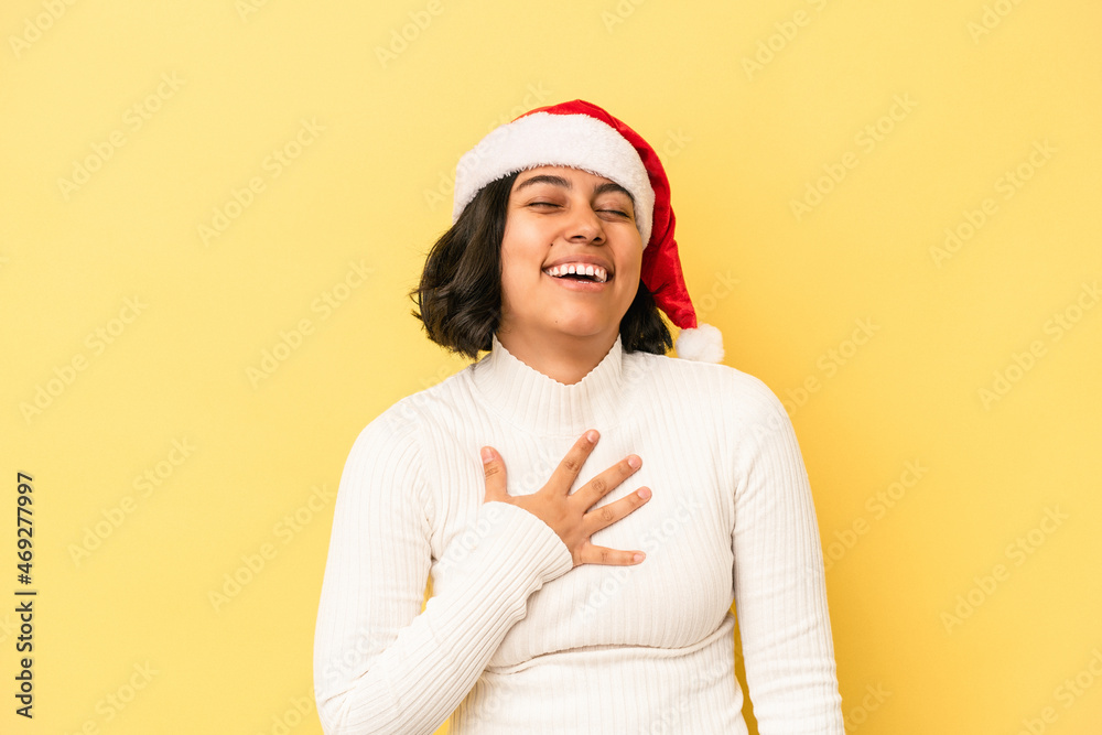 Young latin woman celebrating christmas isolated on yellow background laughs out loudly keeping hand on chest. Young latin woman celebrating christmas isolated on yellow background laughs out loudly keeping hand on chest.