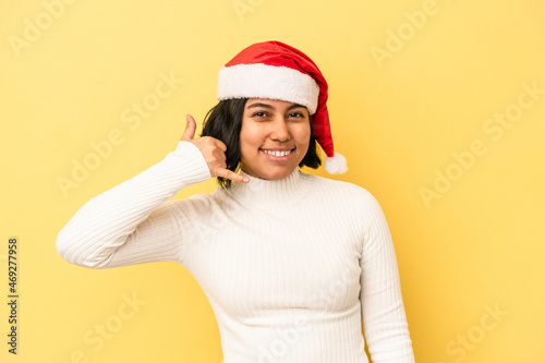 Young latin woman celebrating christmas isolated on yellow background showing a mobile phone call gesture with fingers. © Asier