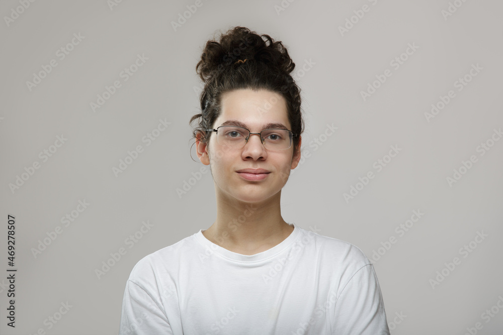 Portrait of a young curly-haired guy with glasses. teenager in white t-shirt on gray background Portrait of a young curly-haired guy with glasses. teenager in white t-shirt on gray background