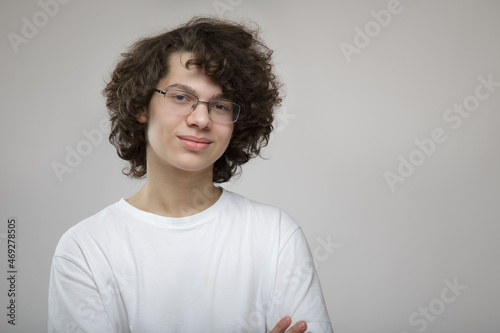 Portrait of a young curly-haired guy with glasses. teenager in white t-shirt on gray background