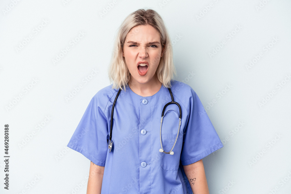 Young nurse woman isolated on blue background screaming very angry and aggressive. Young nurse woman isolated on blue background screaming very angry and aggressive.