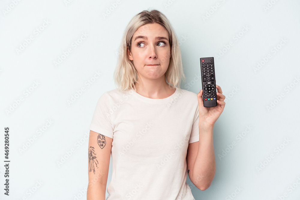 Young caucasian woman holding a tv controller isolated on blue background confused, feels doubtful and unsure. Young caucasian woman holding a tv controller isolated on blue background confused, feels doubtful and unsure.