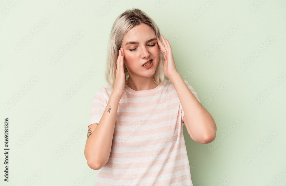 Young caucasian woman isolated on green background touching temples and having headache.