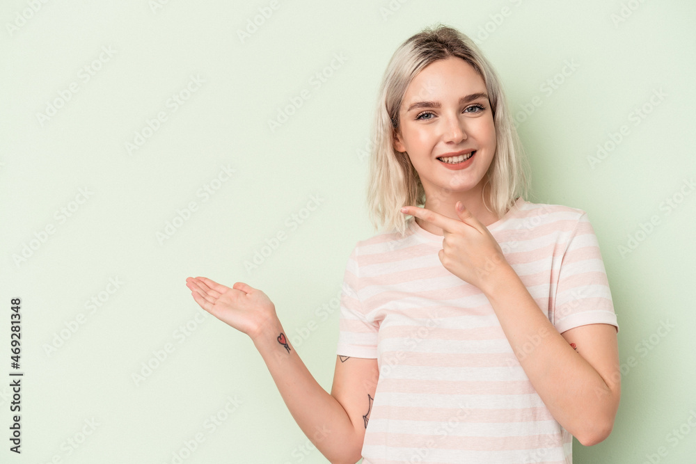 Young caucasian woman isolated on green background excited holding a copy space on palm. Young caucasian woman isolated on green background excited holding a copy space on palm.