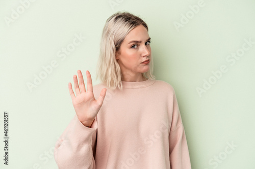 Young caucasian woman isolated on green background rejecting someone showing a gesture of disgust.