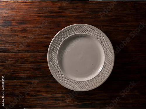 Plato redondo blanco sobre fondo de mesa de madera rústica. Vista cenital. White round plate on rustic wooden table background. Overhead view