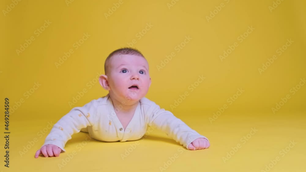 Infant baby boy looks in surprise while lying on his tummy, studio yellow background. Four month old child close up Infant baby boy looks in surprise while lying on his tummy, studio yellow background. Four month old child close up