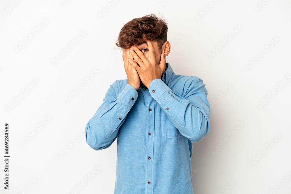 Young mixed race man isolated on grey background blink at the camera through fingers, embarrassed covering face. Young mixed race man isolated on grey background blink at the camera through fingers, embarrassed covering face.