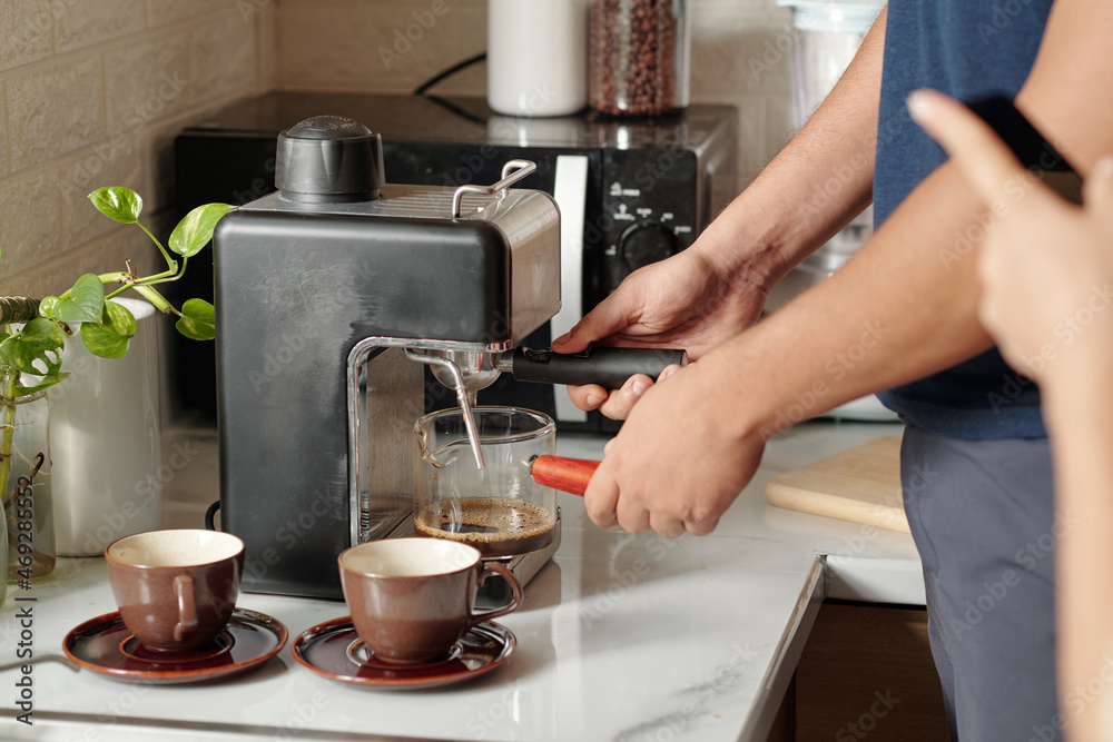 Hands of man using coffee machine when making coffee for himself and girlfriend