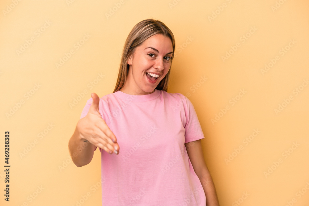Young caucasian woman isolated on yellow background stretching hand at camera in greeting gesture. Young caucasian woman isolated on yellow background stretching hand at camera in greeting gesture.