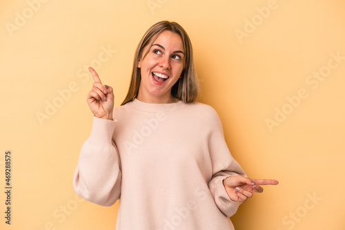 Young caucasian woman isolated on yellow background pointing to different copy spaces, choosing one of them, showing with finger.