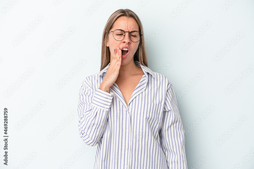 Young caucasian woman isolated on blue background yawning showing a tired gesture covering mouth with hand.