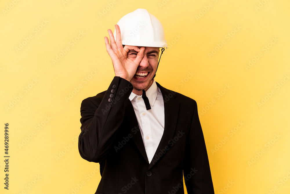 Young architect caucasian man isolated on yellow background excited keeping ok gesture on eye.