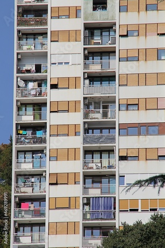 post-communist block, block with lots of balconies and windows, high skyscraper, windows covered with roller shutters, laundry hanging on balconies