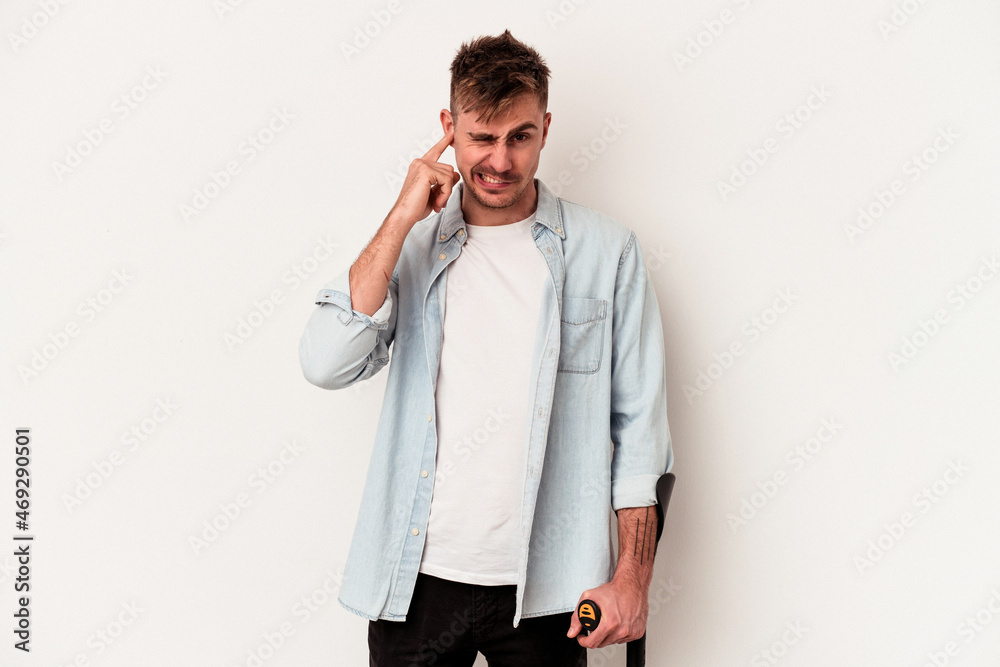 Young caucasian man holding crutch isolated on white background covering ears with hands. Young caucasian man holding crutch isolated on white background covering ears with hands.