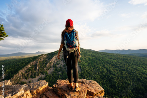 A young female tourist with a backpack admires the sunset from the top of the mountain. A traveler on the background of mountains. A traveler on the background of mountains at sunset. Copy space