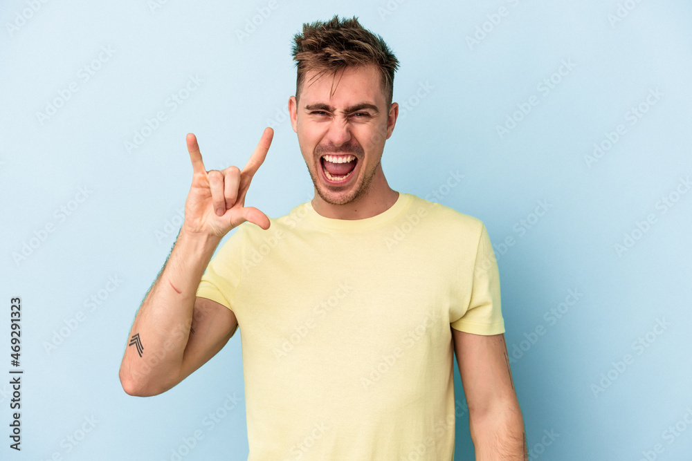 Young caucasian man isolated on blue background showing a horns gesture as a revolution concept. Young caucasian man isolated on blue background showing a horns gesture as a revolution concept.
