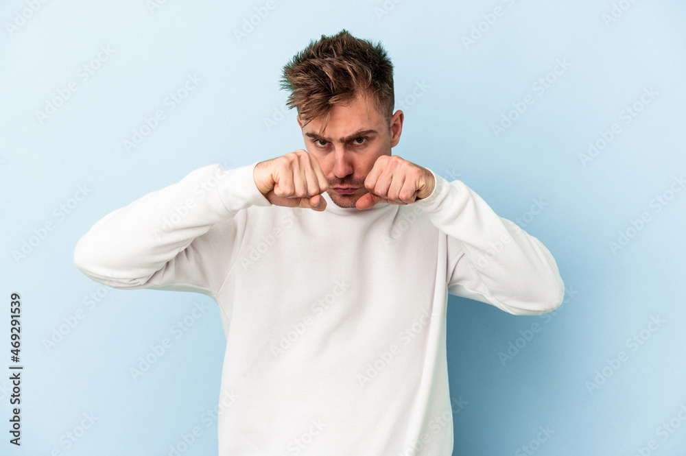 Young caucasian man isolated on blue background throwing a punch, anger, fighting due to an argument, boxing. Young caucasian man isolated on blue background throwing a punch, anger, fighting due to an argument, boxing.