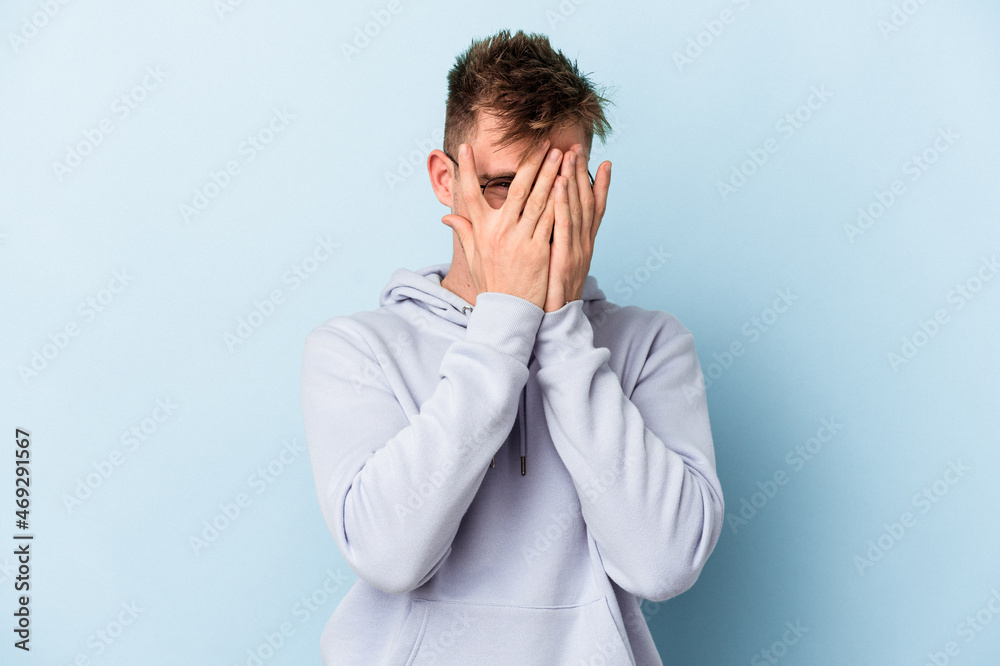 Young caucasian man isolated on blue background blink through fingers frightened and nervous. Young caucasian man isolated on blue background blink through fingers frightened and nervous.