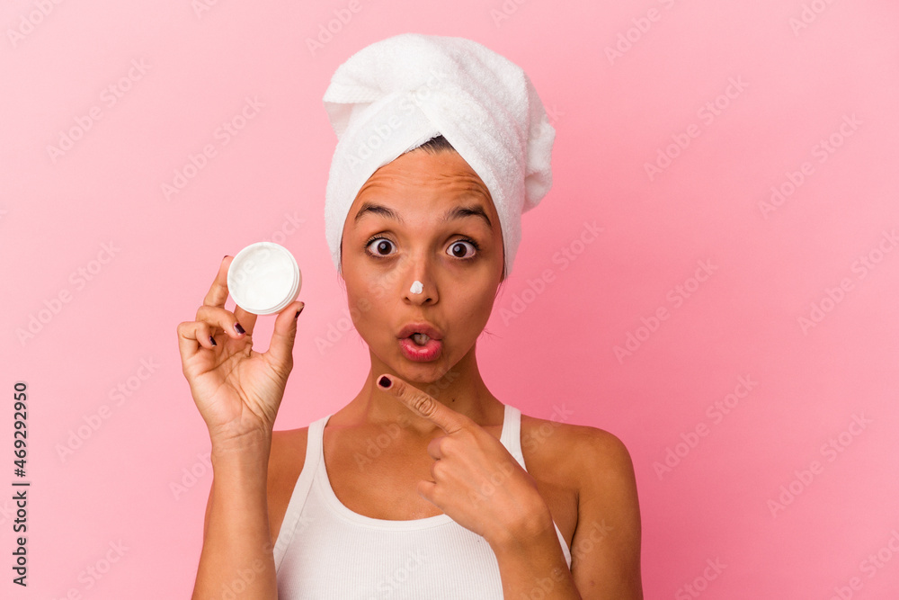 Young mixed race woman holding facial cream isolated on pink background pointing to the side Young mixed race woman holding facial cream isolated on pink background pointing to the side