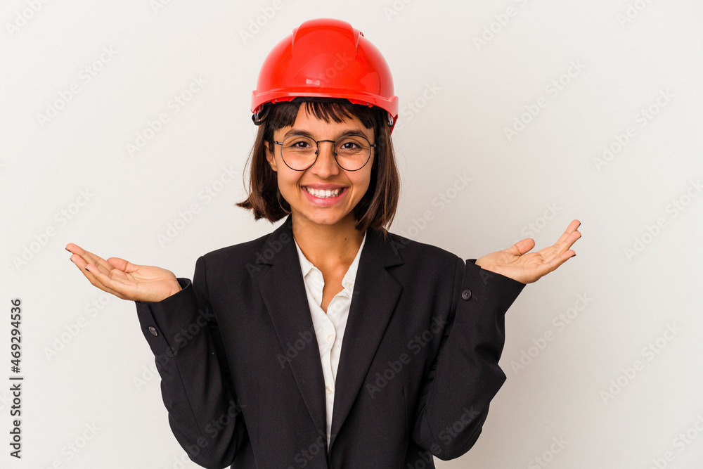 Young architect woman with red helmet isolated on white background makes scale with arms, feels happy and confident. Young architect woman with red helmet isolated on white background makes scale with arms, feels happy and confident.