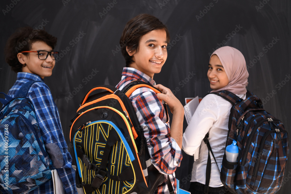 Arabic teenagers, students group portrait against black chalkboard wearing backpack and books in school.Selective focus Arabic teenagers, students group portrait against black chalkboard wearing backpack and books in school.Selective focus