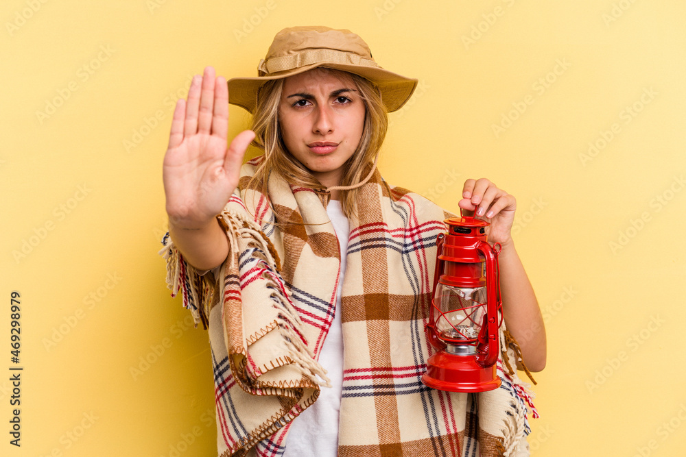 Young caucasian holding lantern isolated on yellow background standing with outstretched hand showing stop sign, preventing you. Young caucasian holding lantern isolated on yellow background standing with outstretched hand showing stop sign, preventing you.