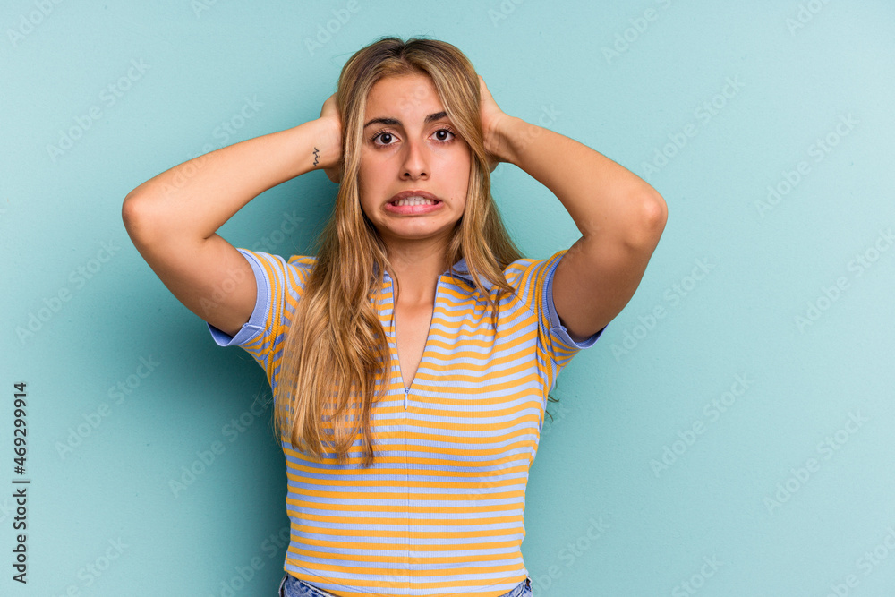 Young caucasian blonde woman isolated on blue background  covering ears with hands trying not to hear too loud sound.