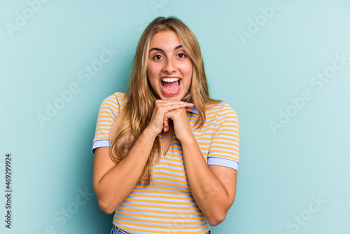 Young caucasian blonde woman isolated on blue background praying for luck, amazed and opening mouth looking to front.