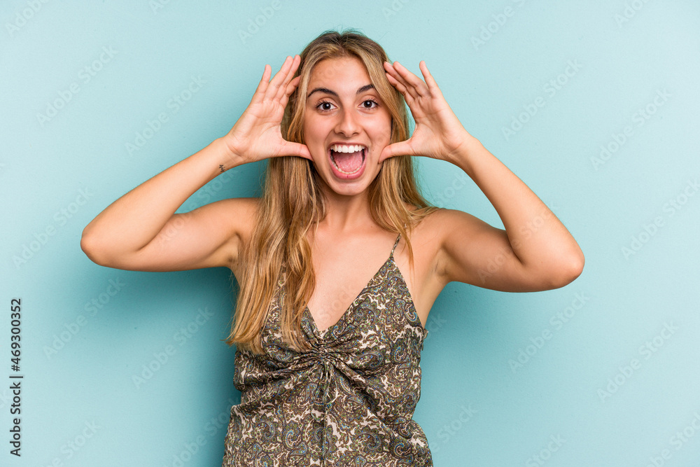 Young caucasian blonde woman isolated on blue background  receiving a pleasant surprise, excited and raising hands.