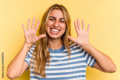 Young caucasian blonde woman isolated on yellow background showing number ten with hands.