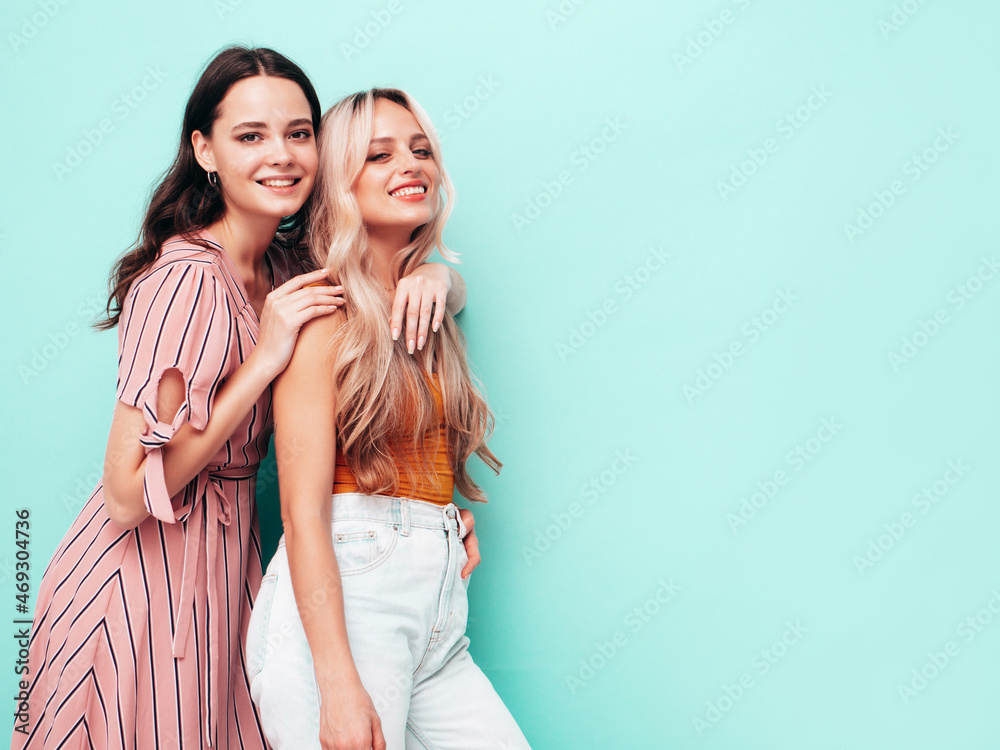 Two young beautiful smiling brunette hipster female in trendy summer clothes. Sexy carefree women posing near blue wall. Positive models having fun. Cheerful and happy Two young beautiful smiling brunette hipster female in trendy summer clothes. Sexy carefree women posing near blue wall. Positive models having fun. Cheerful and happy