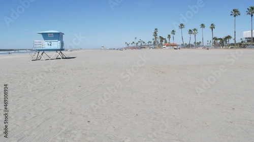Tropical palm trees on white sandy beach by sea water waves, pacific ocean coast, Oceanside California USA. Blue sky and lifeguard tower. Life guard watchtower hut, summertime shore. Los Angeles vibes