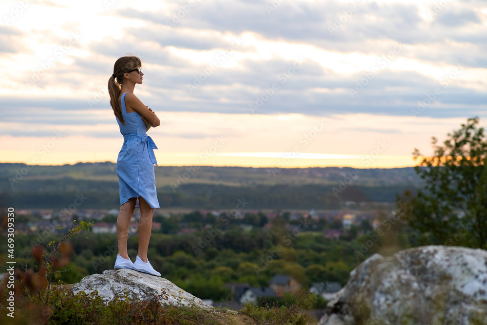 Dark silhouette of a young woman standing on a stone enjoying sunset view outdoors in summer